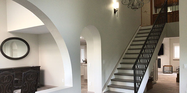 Interior view of a modern home featuring an arched doorway, stairway with metal railing, and neutral-colored walls.