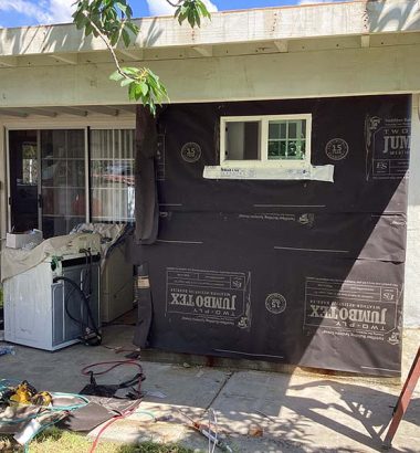 A house with a window and door covered in black tarp, indicating possible repairs or renovations.