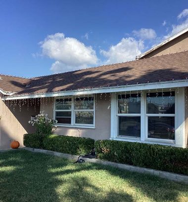 A house with a well-maintained yard and lush green lawn, surrounded by trees and a clear blue sky.