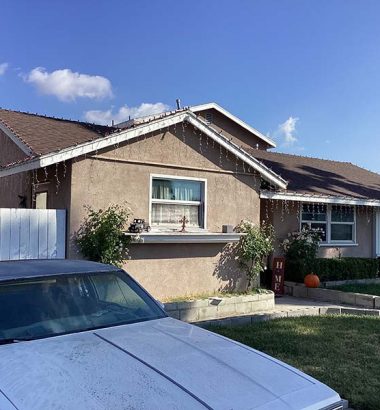 A house with a well-maintained yard and lush green lawn, surrounded by trees and a clear blue sky.