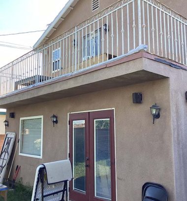 A house featuring a balcony and a ladder leaning against it, set against a clear blue sky.