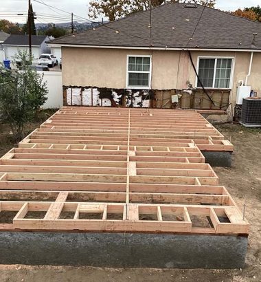 A backyard under construction featuring a wooden deck being built. Tools and materials are visible around the site.