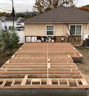 A backyard under construction featuring a wooden deck being built. Tools and materials are visible around the site.