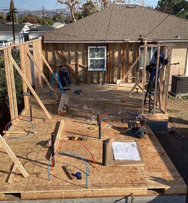 A house under construction featuring a roof and a deck, with scaffolding and building materials visible around it.