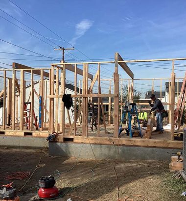 Construction workers are constructing a house in a backyard, surrounded by tools and building materials.