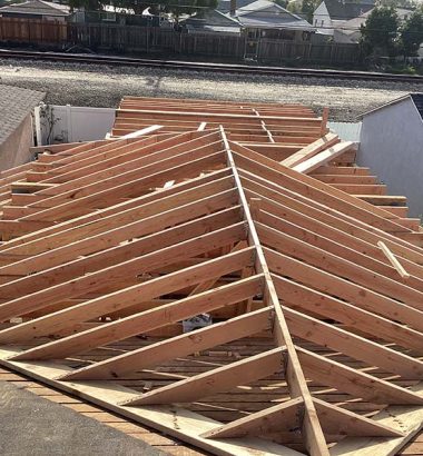 A construction worker assembles wooden beams to create a roof framework on a building site.