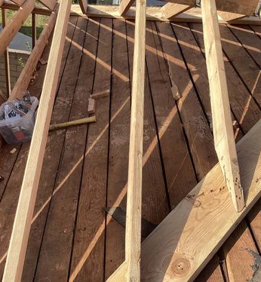 A construction worker assembles wooden beams to create a roof framework on a building site.