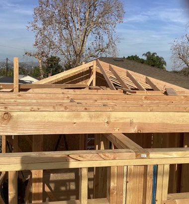 Worker builds a roof in the backyard of a house, with tools and materials visible around the site.
