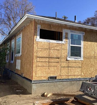 A house under construction, featuring wooden siding and newly installed windows.