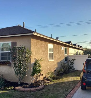 A house with a car parked in front, showcasing a suburban setting with greenery in the background.