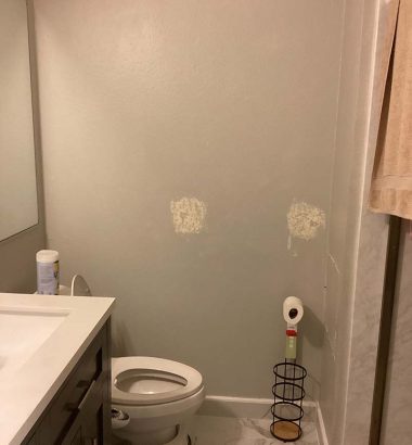 A clean bathroom featuring a toilet, sink, and shower, with neutral-colored tiles and bright lighting.