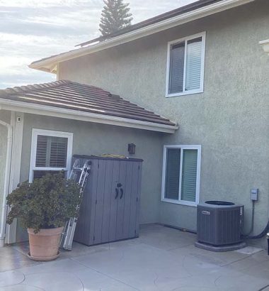 A house featuring a large air conditioner beside a trash can on the side.