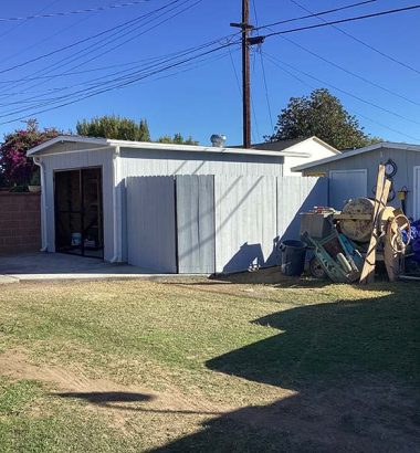 A yard featuring a car parked in front of a house, with green grass and a clear blue sky in the background.