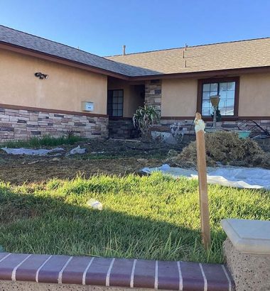 A man is working on home repairs in the yard, surrounded by tools and materials.