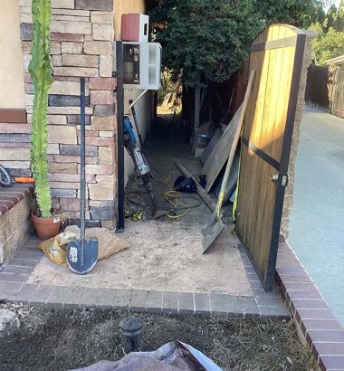 A house with a brick wall stands beside a green cactus plant in a sunny outdoor setting.