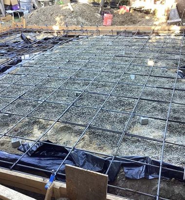 A concrete slab is being poured in a backyard, with workers carefully managing the flow of the wet concrete.