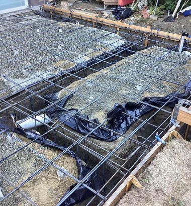 A worker pours concrete into a mold in a backyard, preparing a new slab for construction or landscaping.