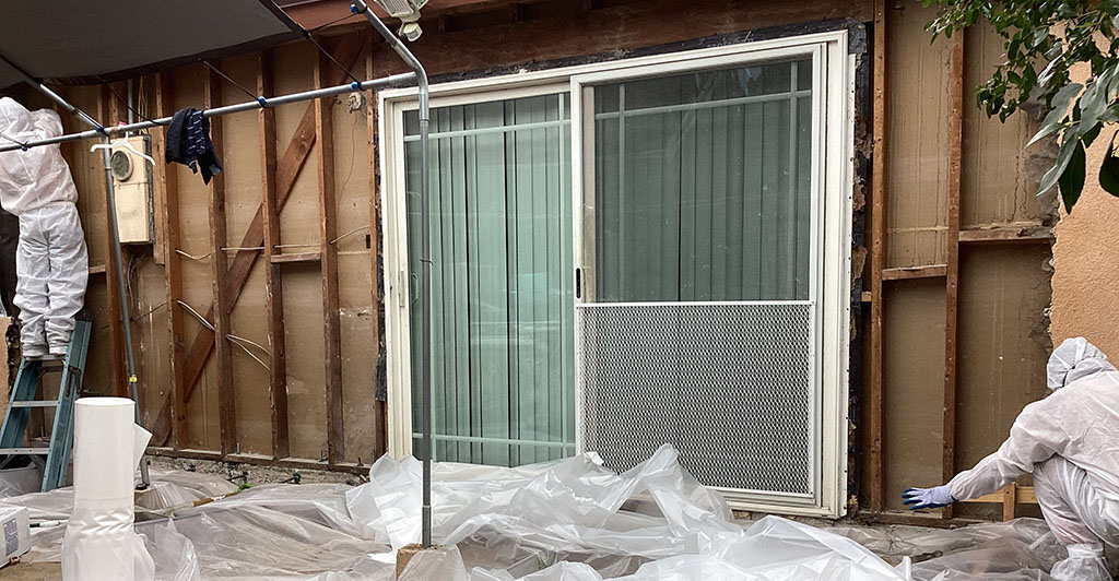 Two men in white suits are collaborating on construction work at a house.